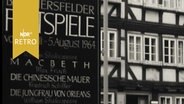 Ankündigungstafel "Bad Hersfelder Festspiele vom 3. Juli - 5. August 1964" in der Hersfelder Innenstadt neben einem Fachwerkhaus  