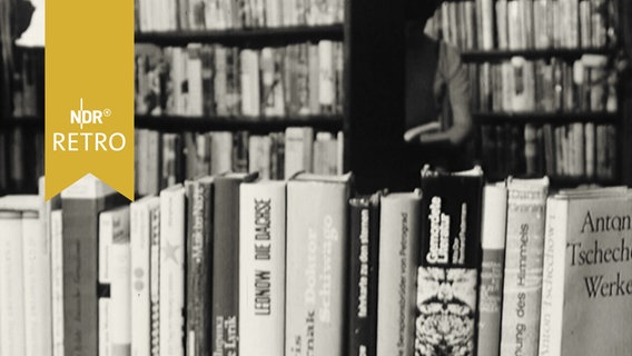 Auf einem Tisch in einer Buchhandlung stehen zahlreiche deutsche Ausgaben russischer und sowjetischer Autoren aufgereiht, dahinter die Regale im Buchladen (1964)  