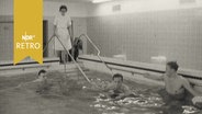 Männer beim Schwimmen in einem Krankenhausschwimmbad unter Beoachtung einer Krankenschwester (1964)  