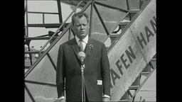 Willy Brandt spricht vor einer Flugzeugtreppe in ein Mikrofon.  