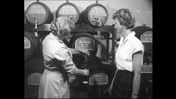 Zwei Frauen zapfen Wein aus Weinfässern.  