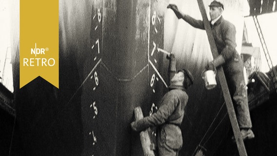 Zwei Arbeiter beim Anstreichen eines Schiffsbugs in einer Werft 1965  
