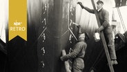 Zwei Arbeiter beim Anstreichen eines Schiffsbugs in einer Werft 1965  