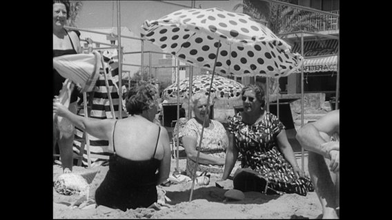 Deutsche Urlauber:innen in Strandkleidung am Strand.  