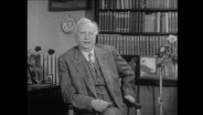 Karl Jaspers sitzt vor einem Bücherregal.  