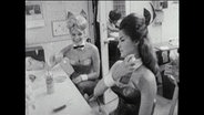 Zwei Frauen im Playboy-Kostüm frisieren sich.  