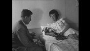 Reporter interviewt eine Frau in einem Krankenhaus-Bett.  