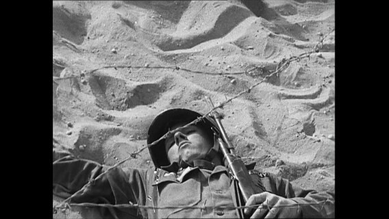 Soldat robbt unter Stacheldraht im Sand.  