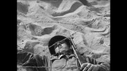 Soldat robbt unter Stacheldraht im Sand.  