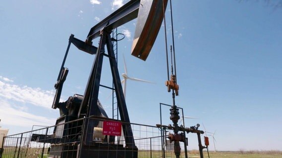 Eine Ölförderanlage und im  Hintergrund ein Windrad  