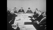 Männer sitzen an einem langen Konferenz-Tisch.  