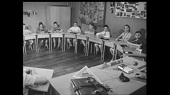 Schulkinder sitzen an Tischen in einem Halbkreis (Archiv-Bild).  