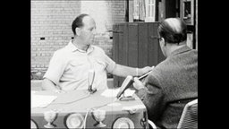 Zwei Männer sitzen an einem Tisch und sprechen in Mikrofone.  