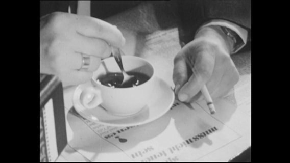 Kaffee in einer Tasse wird umgerührt, in der einen Hand eine Zigarette.  