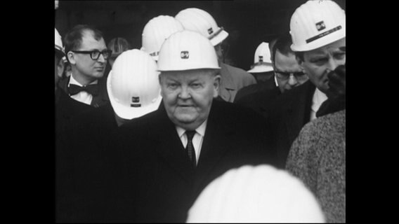 Der Politiker Ludwig Erhard trägt einen Helm und ist von mehreren Arbeitern umgeben (Archivbild)  