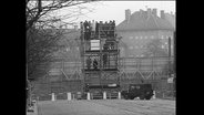 Menschen stehen auf einer Aussichtsplattform an der Bernauer Straße und schauen über die Mauer.  