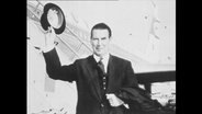 Gerhard Schröder steht vor einem Flugzeug und hebt seinen Hut.  