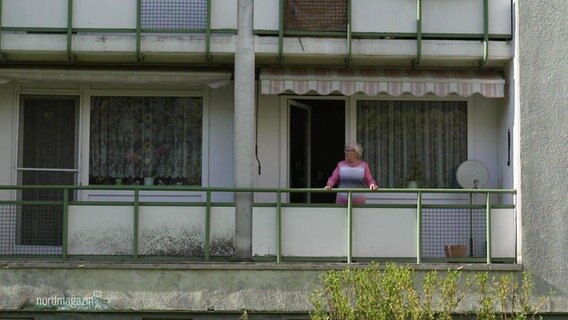 Eine Frau steht auf dem Balkon ihrer Wohnung in einem Mehrfamilienhaus.  