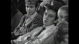 Drei Schüler sitzen in einem Hörsaal.  