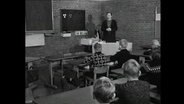Eine Lehrerin steht im Klassenzimmer vor einer Schulklasse.  
