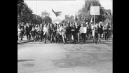 Demonstrierende laufen mit Plakaten über eine Straße  