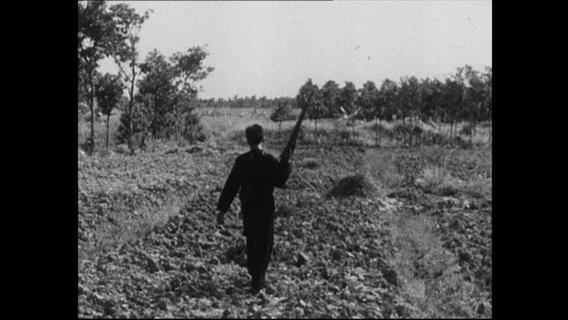 Ein Mann mit einem Gewehr läuft über ein Feld  