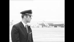 Ein Pilot steht auf einem Rollfeld, im Hintergrund stehen Flugzeuge.  
