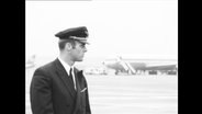 Ein Pilot steht auf einem Rollfeld, im Hintergrund stehen Flugzeuge.  