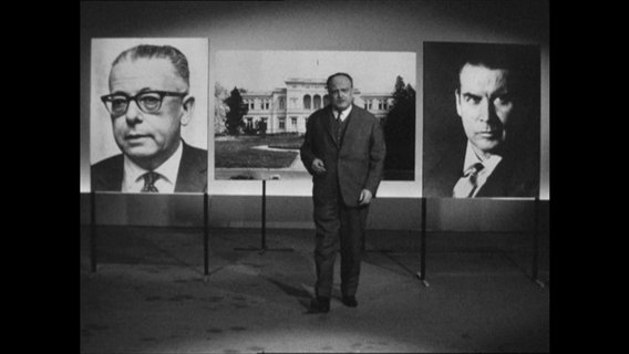 Sebastian Haffner steht vor den Bildern Schröders, Heinemanns und des Bonner Palais Schaumburg.  