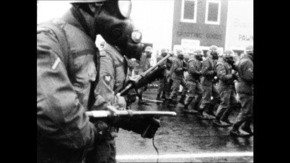 Soldaten mit Gasmasken und Gewehren laufen in einer Reihe  