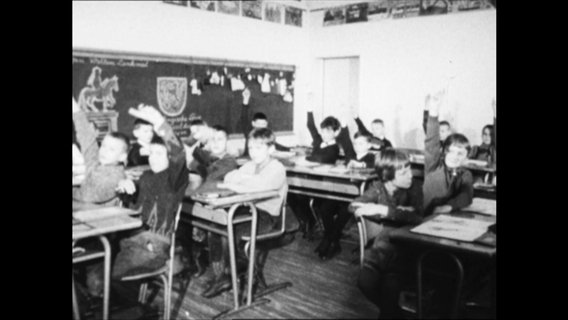Schüler in einem Klassenzimmer heben die Hand  