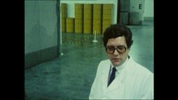 Ein Mann in einem weißen Kittel steht in einer Halle vor gelben Fässern (Archivbild).  