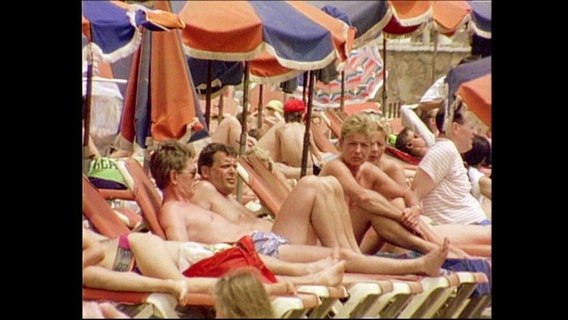 Menschen sonnen sich am Strand auf Liegestühlen.  