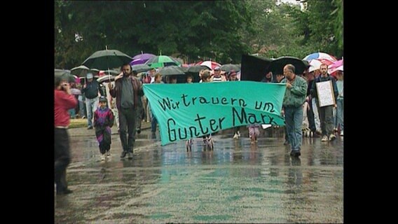 Teilnehmer eines Trauermarschs, die das Banner "Wir trauern und Guter Marx" halten.  