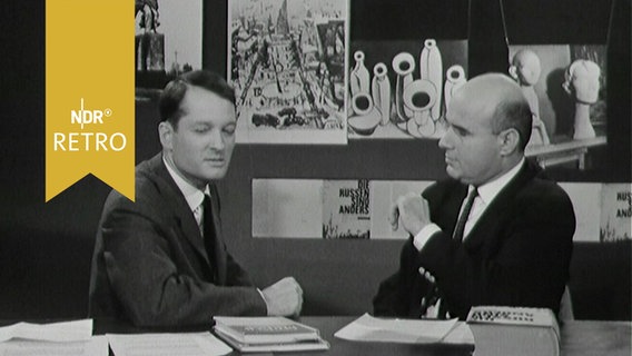 Moderator im Gespräch mit einem Kulturwissenschaftler im Studio vor einer Wand mit Werken des Futurismus (1963)  