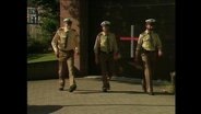 Drei Polizeieamte laufen in ihrer Uniform über den Gehweg  