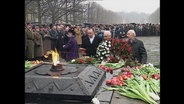 Männer legen Blumenkränze an einem Gedenkort nieder.  