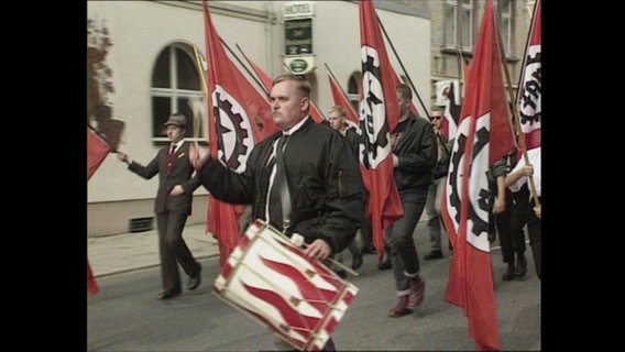 Rechtsradikale laufen mit Trommeln und Fahnen über eine Straße.  