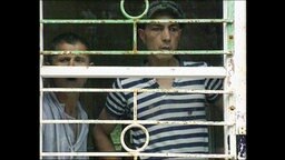 Zwei Männer schauen durch das Gitterfenster einer rumänischen Psychiatrie.  