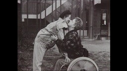 Eine Frau und ein Mann, der im Rollstuhl sitzt, küssen sich.  