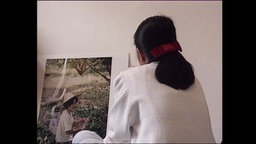 Eine Frau sitzt mit dem Rücken zur Kamera vor einer Wand.  