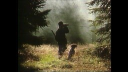 Ein Jäger steht mit seinem Jagdhund im Wald.  