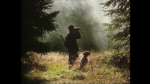 Ein Jäger steht mit seinem Jagdhund im Wald.  