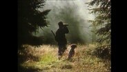 Ein Jäger steht mit seinem Jagdhund im Wald.  