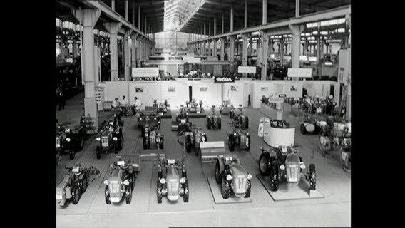 Zahlreiche Traktoren in einer Messehalle zur Ausstellung (1964)  