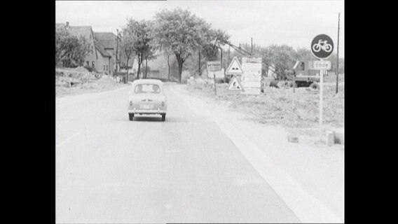 Ein Auto fährt auf einer Landstraße in ein Dorf (1964)  