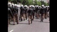 Dutzende Polizisten in Uniform und Schutzkleidung laufen auf einer Straße (Archivbild).  