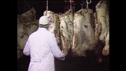 Ein Mann in weißem Kittel prüft Fleisch in einer Kühlhalle (Archivbild).  
