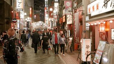 Eine Einkaufsstraße mit zahlreichen Leuchtreklamen in Tokio.  