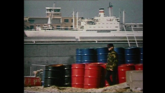 Schwarze, blaue und rote Fässer stehen vor einem Schiff (Archivbild).  